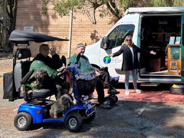 2 people using their mobility aids. Behind them is another person next to a van with an open sliding door.